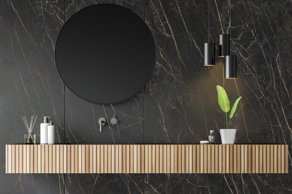 Close up of wooden bathroom sink with round mirror above it located in room with black marble walls and original lamps. 3d rendering